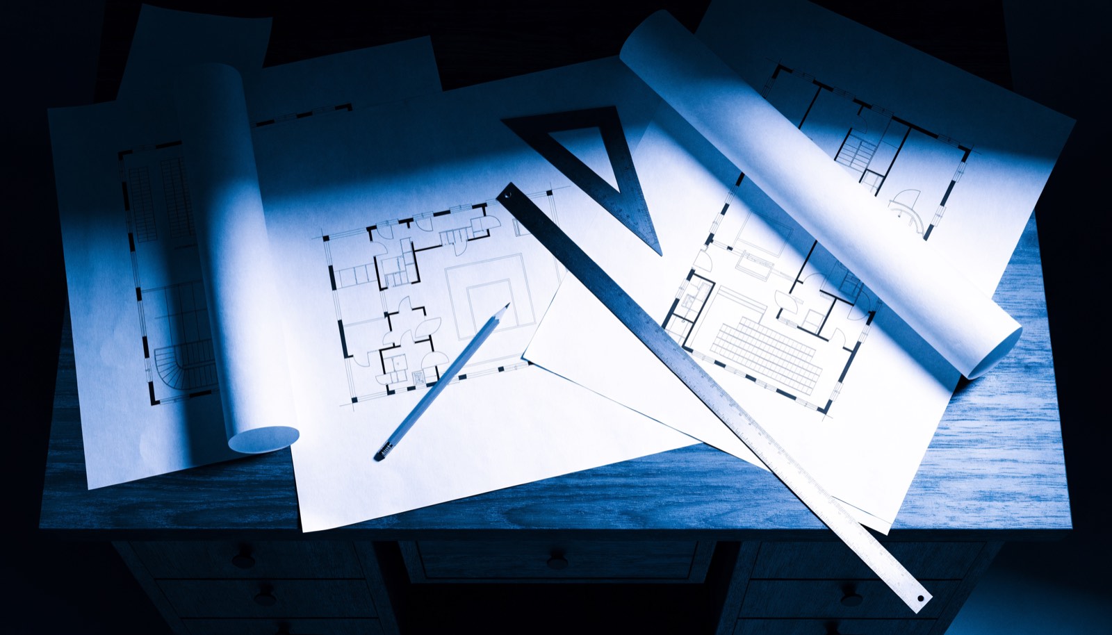 Architectural floor plans and drafting tools on a work table, in dark blueprint tones