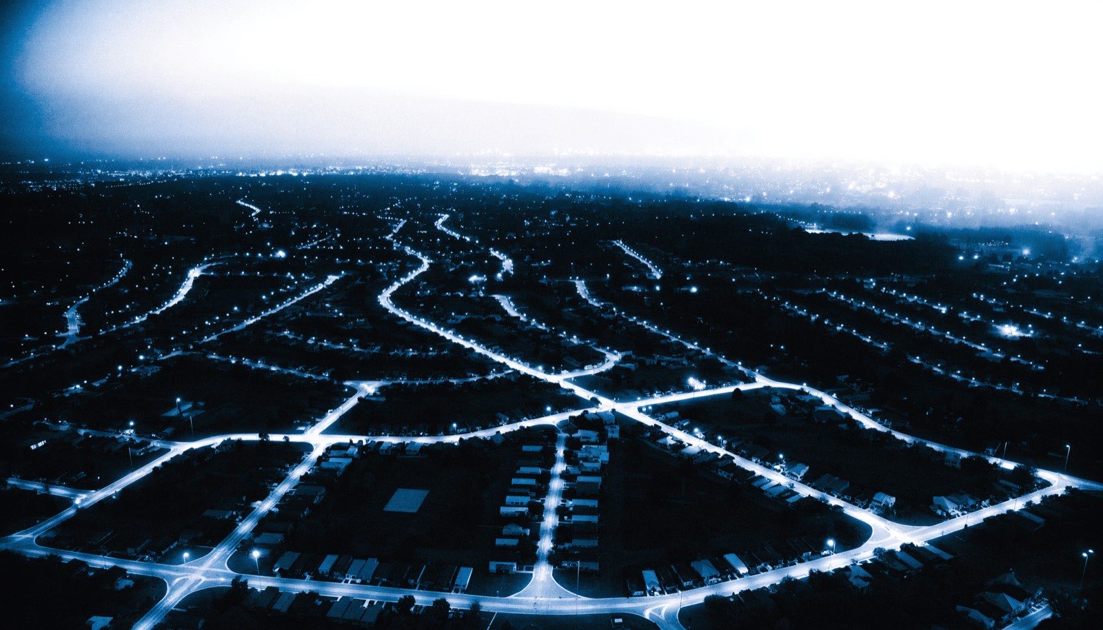 Aerial view of a suburban street grid at dusk, streets glowing like blueprint linework
