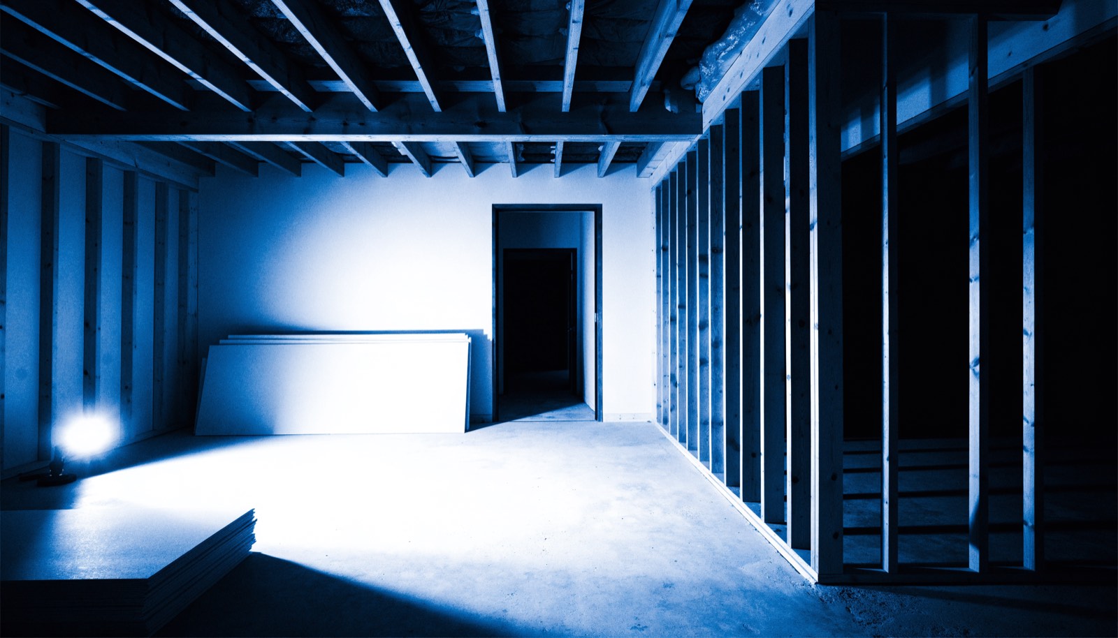 A garage interior mid-conversion with exposed stud framing, in dark blueprint tones