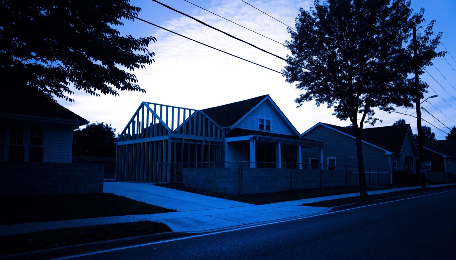 New wall framing of a home addition rising against an existing roofline, in dark blueprint tones